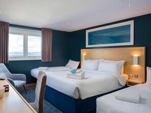 Habitación de hotel con una cama grande, un escritorio y una silla. Hay una ventana con cortinas, un cuadro en la pared y una lámpara en el techo.