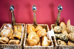 Eine Auswahl an Backwaren in einem Korb, darunter Croissants und Brötchen.