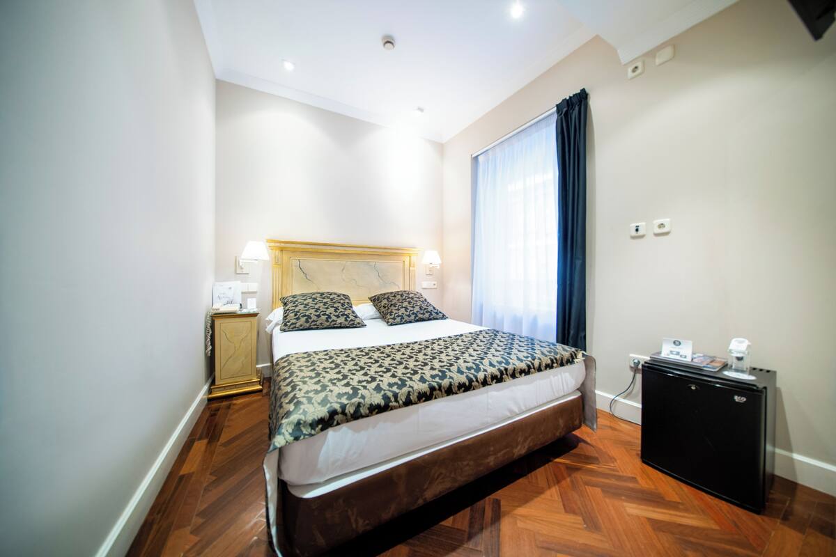 Habitación de hotel con una cama grande, una mesita de noche, un escritorio y una ventana con cortinas.