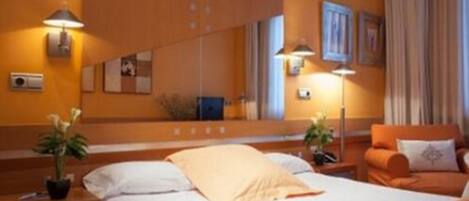 Ein Hotelzimmer mit Bett, Nachttischen, einer Lampe, einem Sessel und einem großen Spiegel.