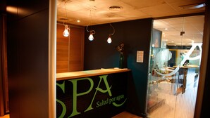 Ein Empfangsbereich mit einer Rezeption, die „SPA Salud por agua“ heißt, einer Holztresen und einer Glastrennwand.