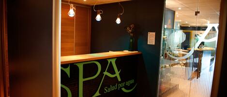 A reception area with a reception desk labeled "SPA Salud por agua," a wooden counter, and a glass partition.