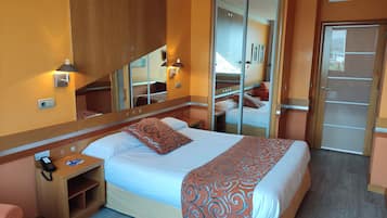 A hotel room with a bed, bedside table, phone, mirror, and wardrobe.