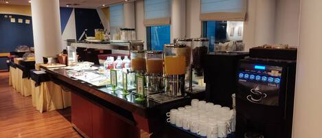 A buffet setup with various food and drink options, including a coffee machine and beverage dispensers.