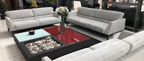 A modern living room with two white sofas, a glass coffee table with a red top, and a vase with flowers.