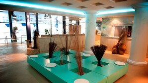Eine moderne Lobby mit einem türkisblauen Empfangstresen, weißen Säulen und Zimmerpflanzen.