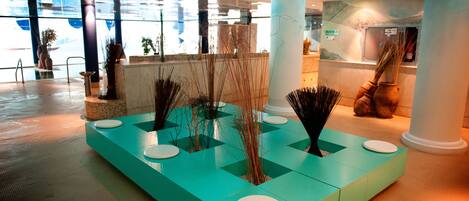 A modern lobby with a teal reception desk, white columns, and indoor plants.
