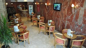 A hotel lobby with marble walls, multiple seating areas with cushioned chairs, a coffee machine, and a refrigerator stocked with beverages. - Gawharet Al Ahram Hotel (Giza)
