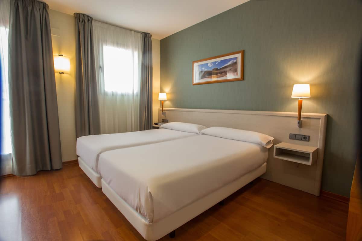 A double bed with a headboard, two bedside tables with lamps, a nightstand, and a framed picture on the wall.