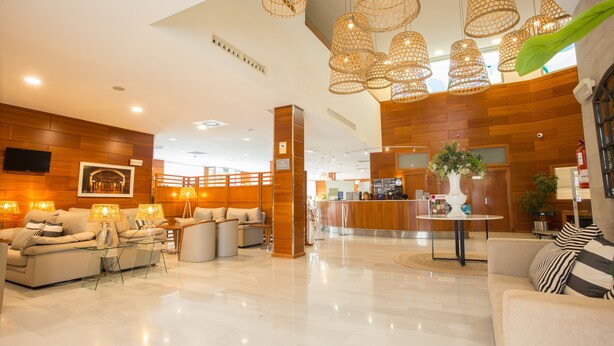 A modern lobby with a reception desk, seating areas, and decorative lighting. - Hotel Alaquas (Alaquas)