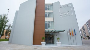 A modern hotel building with a prominent entrance, large potted plants, and multiple flags. - Hotel Alaquas (Alaquas)