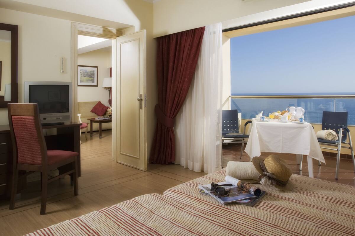 Une chambre d’hôtel avec balcon, télévision, table à manger et vue sur la mer.