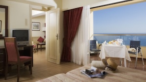 A hotel room with a balcony, a TV, a dining table, and a view of the sea.