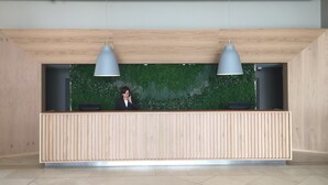 A reception desk with a wooden finish, two pendant lights, and a green wall with a textured pattern.