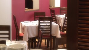 A dining area with tables set for multiple guests, chairs, and a stack of plates.