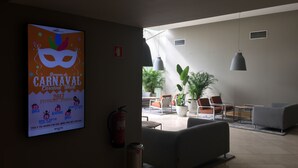 A lobby with a poster advertising Carnaval 2017, a fire extinguisher, and seating areas with potted plants.