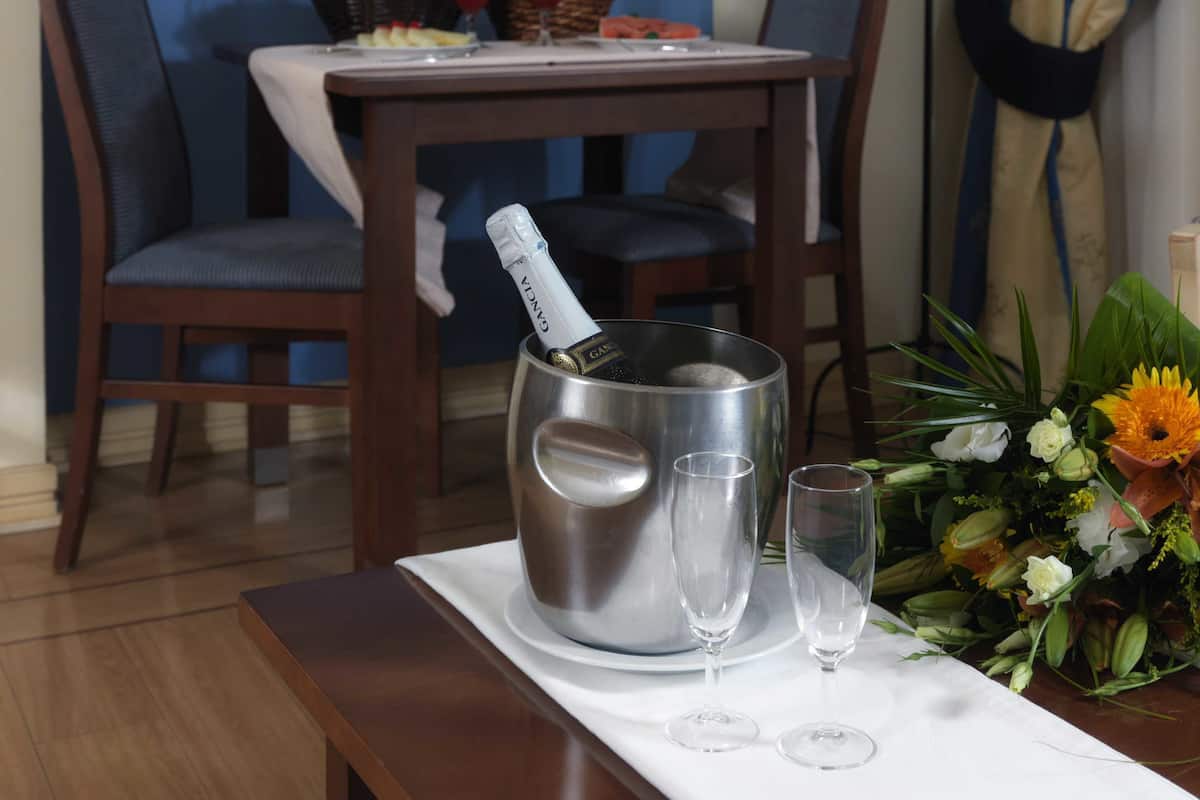 Un coin repas avec une table dressée pour deux personnes, une bouteille de champagne et un vase rempli de fleurs.