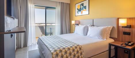 A hotel room with a bed, a desk, a chair, a small table, and a window with curtains.