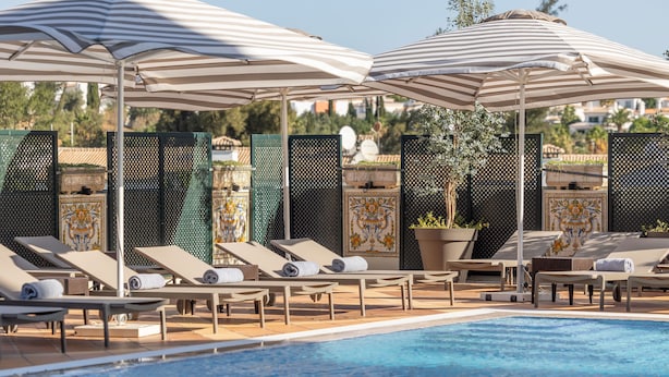 A poolside area with lounge chairs and striped umbrellas. - Holiday Inn Algarve Albufeira by IHG (Albufeira)
