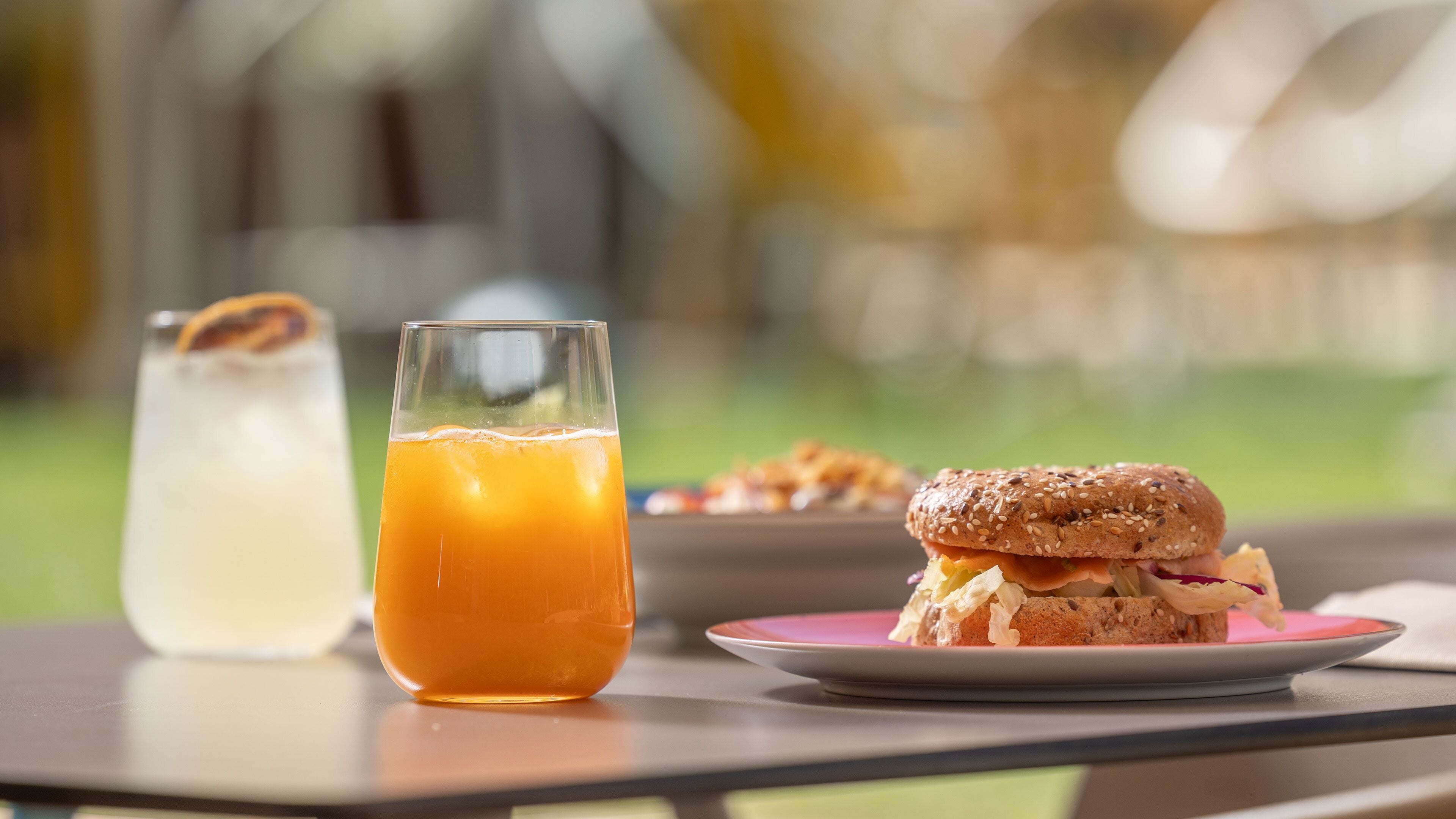 Una mesa con un vaso de jugo de naranja, un sándwich y un plato de comida.