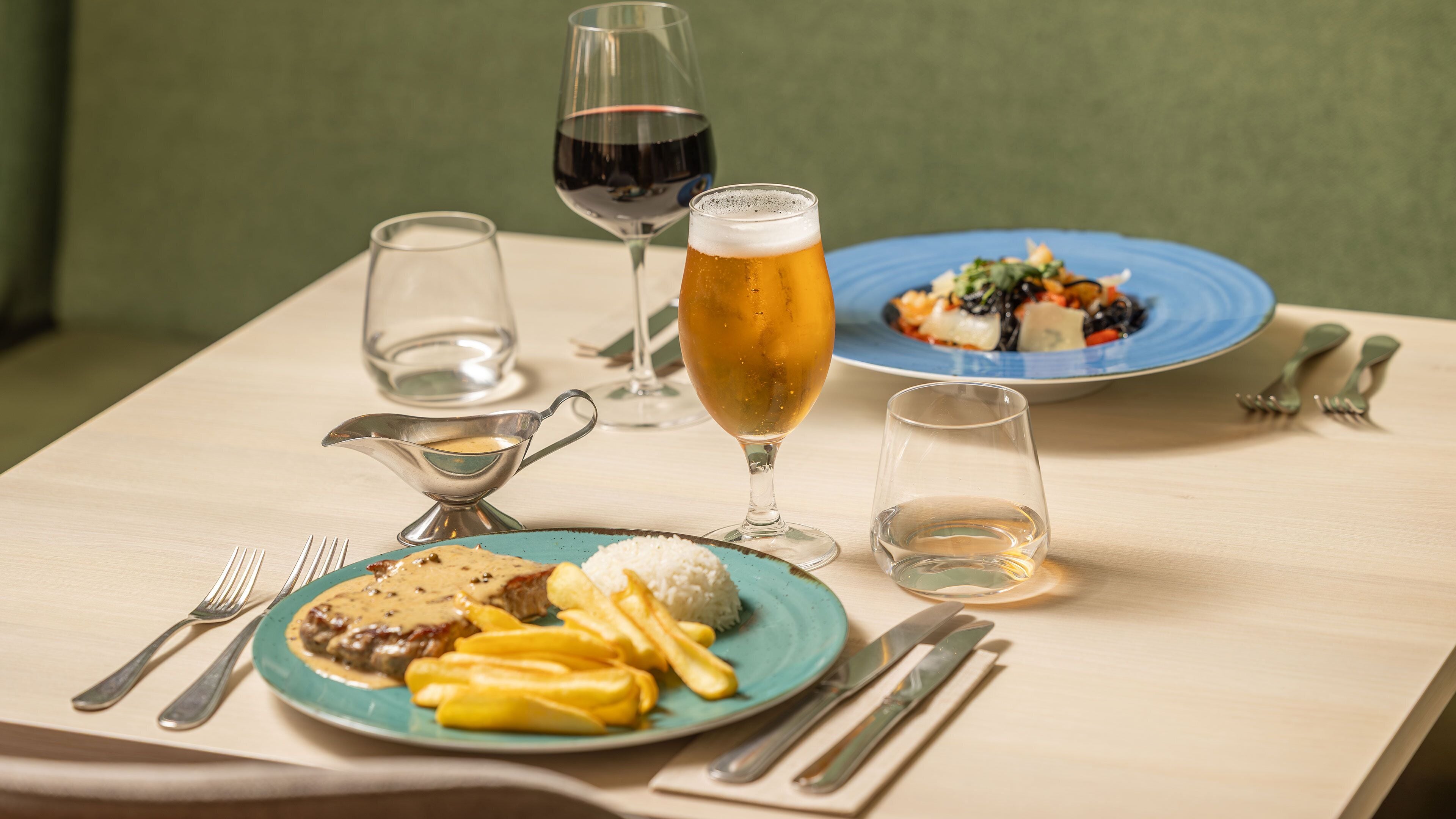 A dining table with plates of food, glasses of beverages, and cutlery.