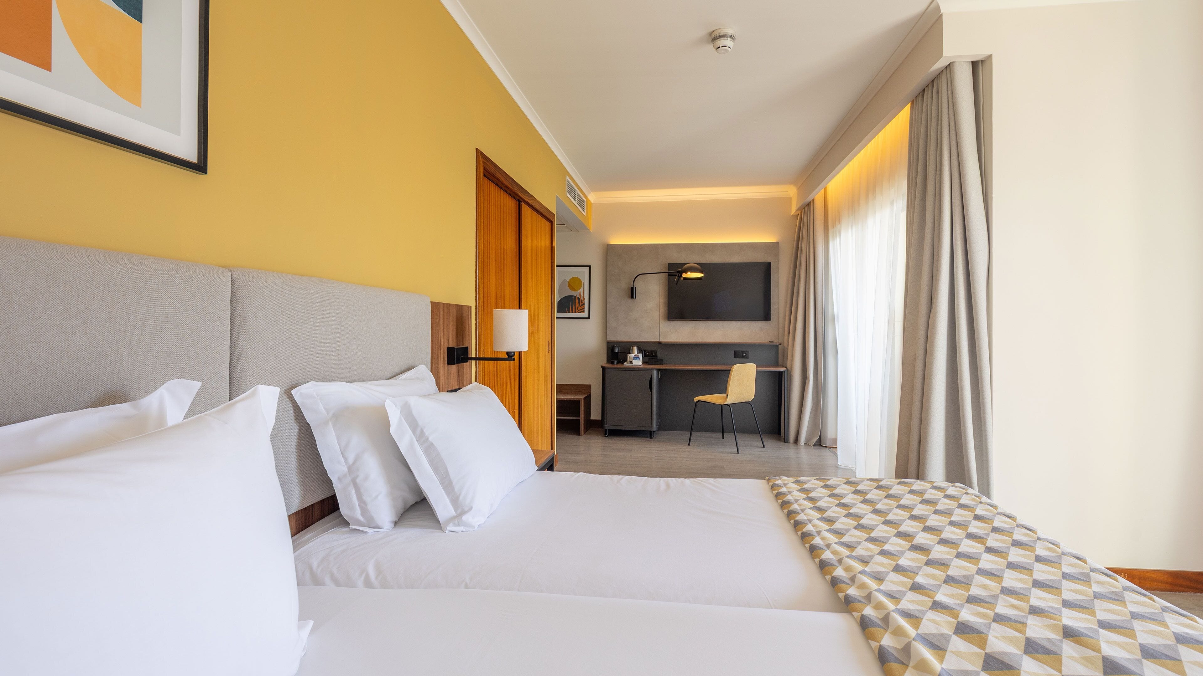 A hotel room with two beds, a kitchenette, a desk, and a chair.