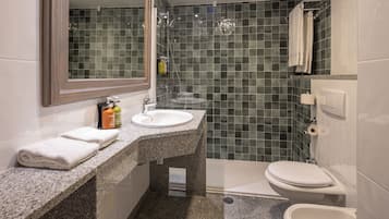 Un baño con encimera de granito, un lavabo blanco, un espejo, cabina de ducha con mampara de vidrio y un inodoro.