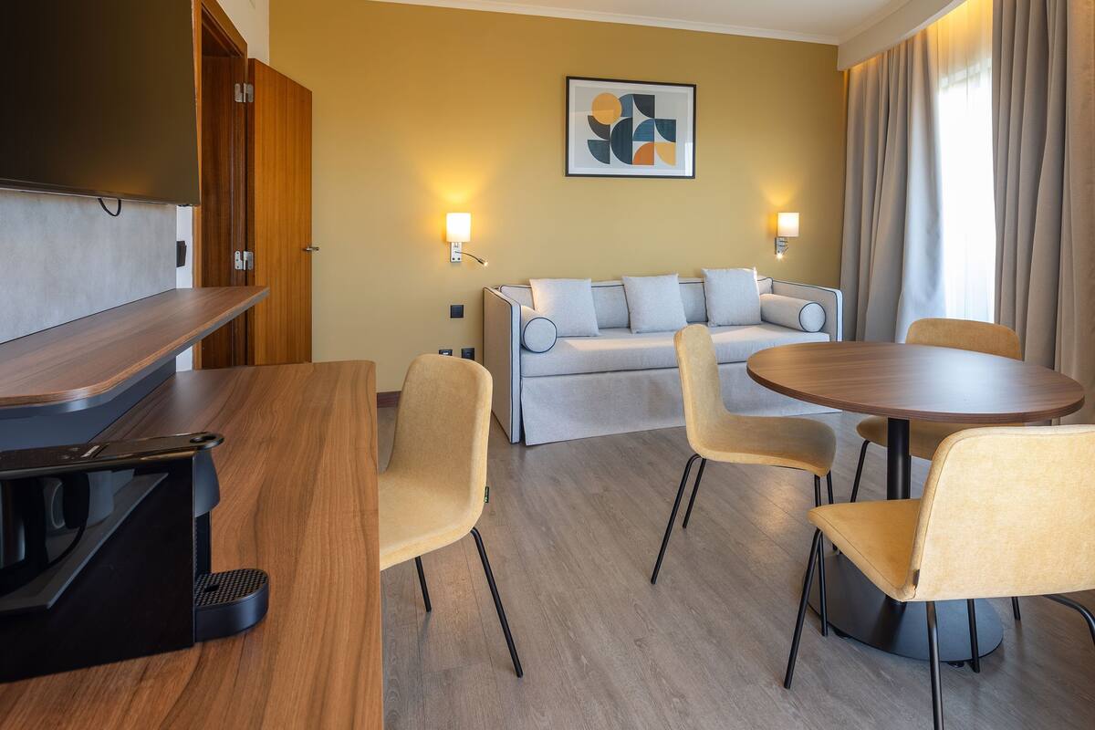 Una habitación de hotel moderna con un escritorio de madera, un sofá y una mesa redonda de comedor.