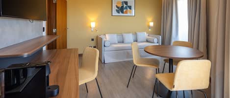 A modern hotel room with a wooden desk, a sofa, and a round dining table.
