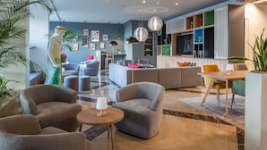 A modern hotel lobby with grey sofas, a wooden dining table, and a large plant. - Holiday Inn Algarve Albufeira by IHG (Albufeira)