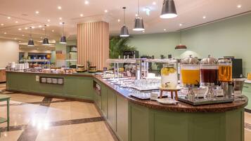 A buffet area with various food and drink options, including a fruit display and beverage dispensers.