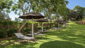 A row of sun loungers with thatched umbrellas in a well-maintained garden. - Holiday Inn Algarve Albufeira by IHG (Albufeira)