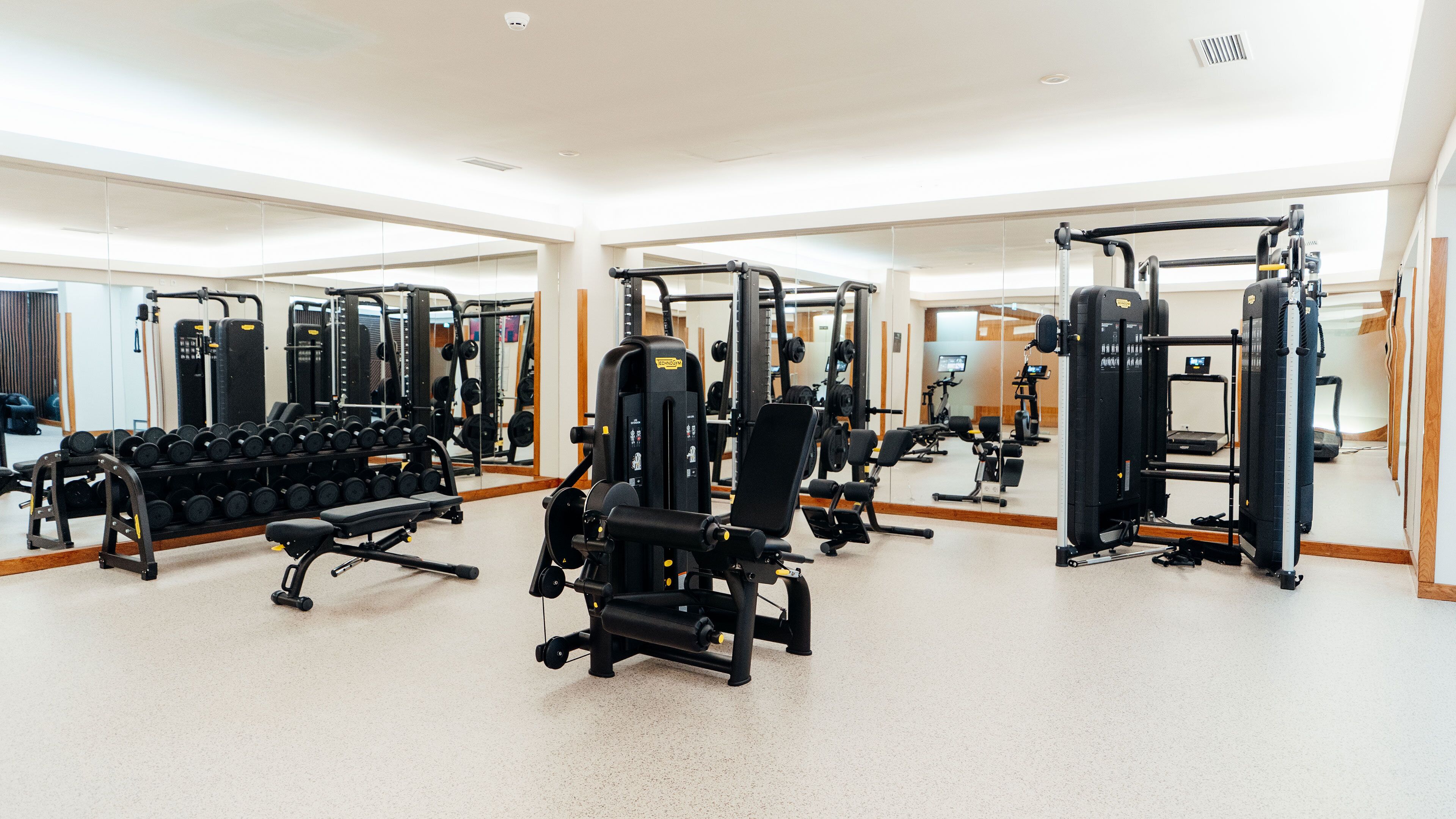 Ein Fitnessstudio mit unterschiedlichen Trainingsgeräten, Spiegeln und einem Gewichtsständer.