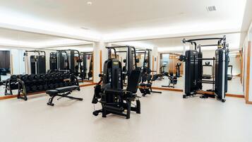 Ein Fitnessstudio mit unterschiedlichen Trainingsgeräten, Spiegeln und einem Gewichtsständer.