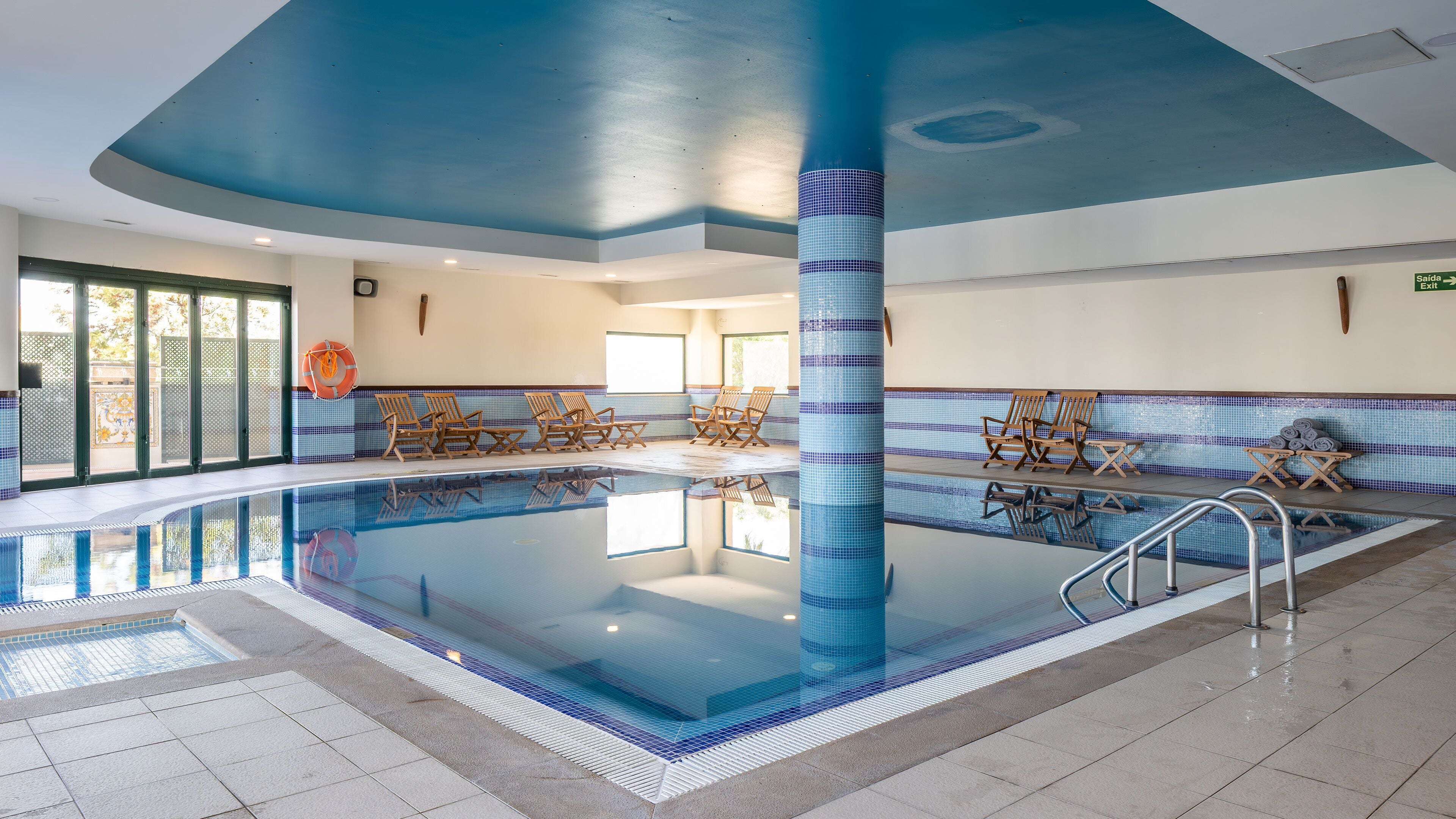 A swimming pool with lounge chairs, a tiled wall, and a clear ceiling.