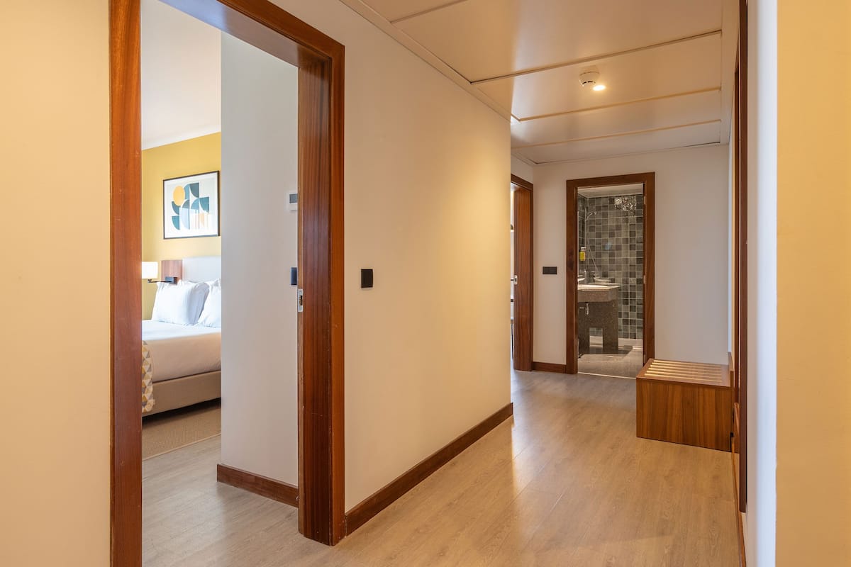 Pasillo de hotel con una cama, un baño con ducha y un pequeño espacio de descanso.