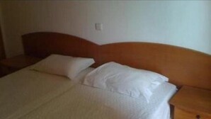 Ein Standard-Hotelzimmer mit Holz-Kopfteil, einem Einzelbett mit weißer Bettwäsche und einem Nachttisch mit Lampe.