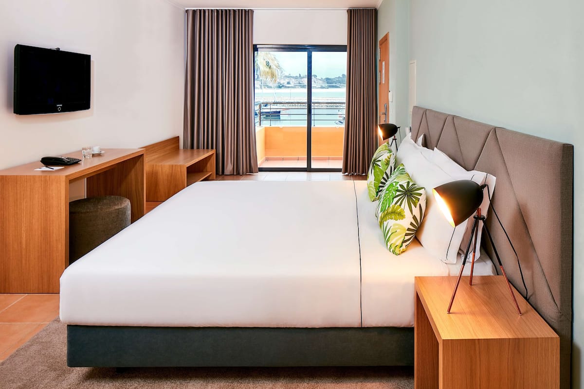 Een moderne hotelkamer met een groot bed, een bureau, een televisie en een balkon met uitzicht op zee.