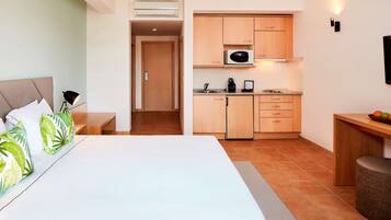 Quarto de hotel com cama, escrivaninha, cozinha compacta e banheiro.