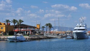 A marina with boats docked, a building with outdoor seating, and palm trees.
