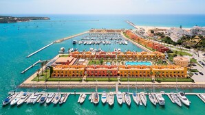 A marina with numerous boats docked, a large swimming pool, and a hotel with orange buildings.