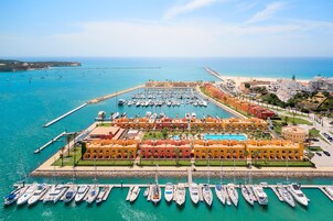 A marina with numerous boats docked, a large swimming pool, and a hotel with orange buildings.