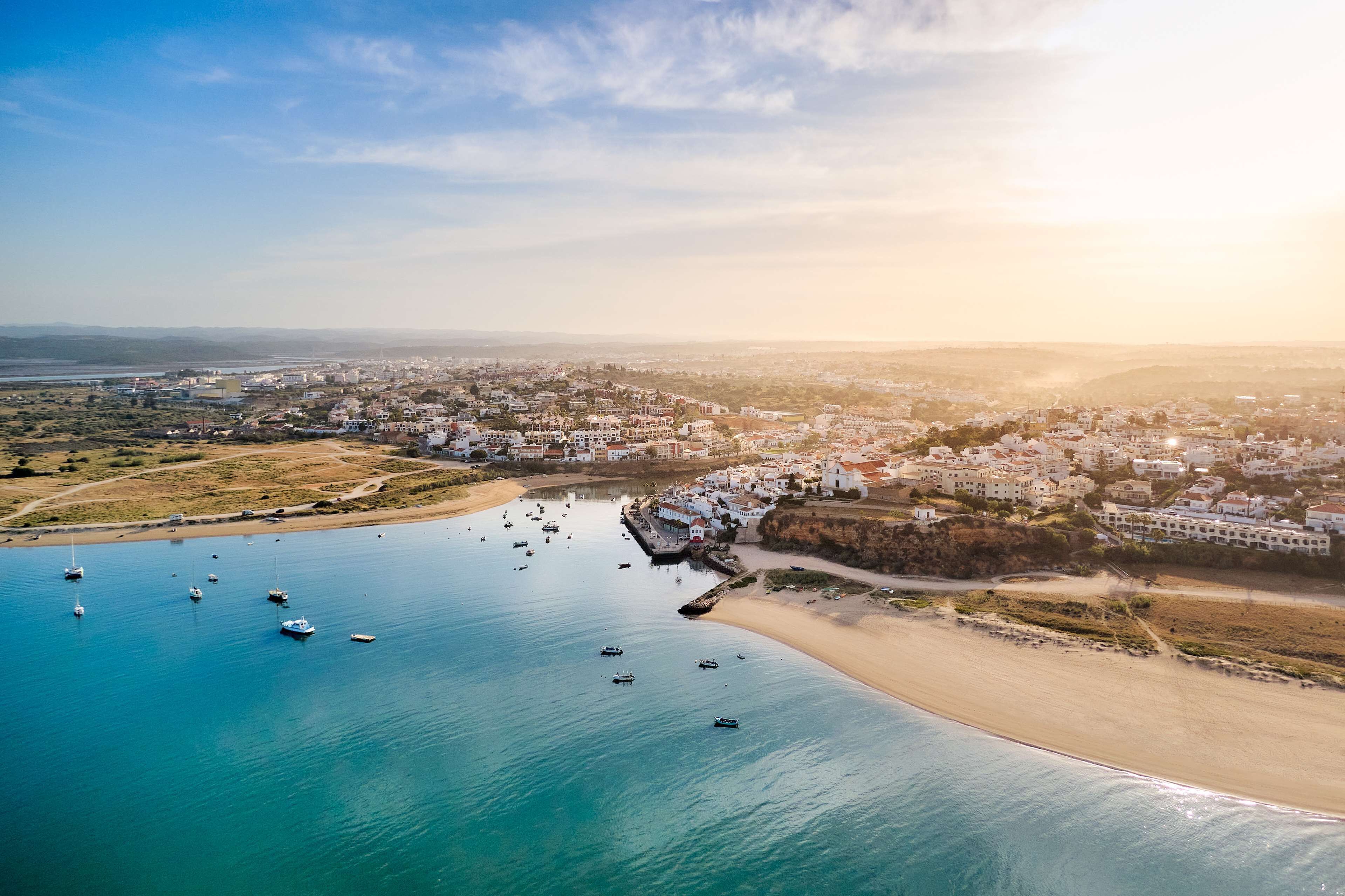 Vista aérea de un pueblo costero con playa, barcos y edificios blancos.
