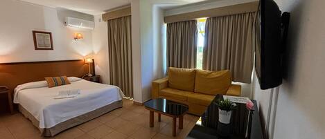 A hotel room with a bed, a sofa, a coffee table, a TV, and a window with curtains.
