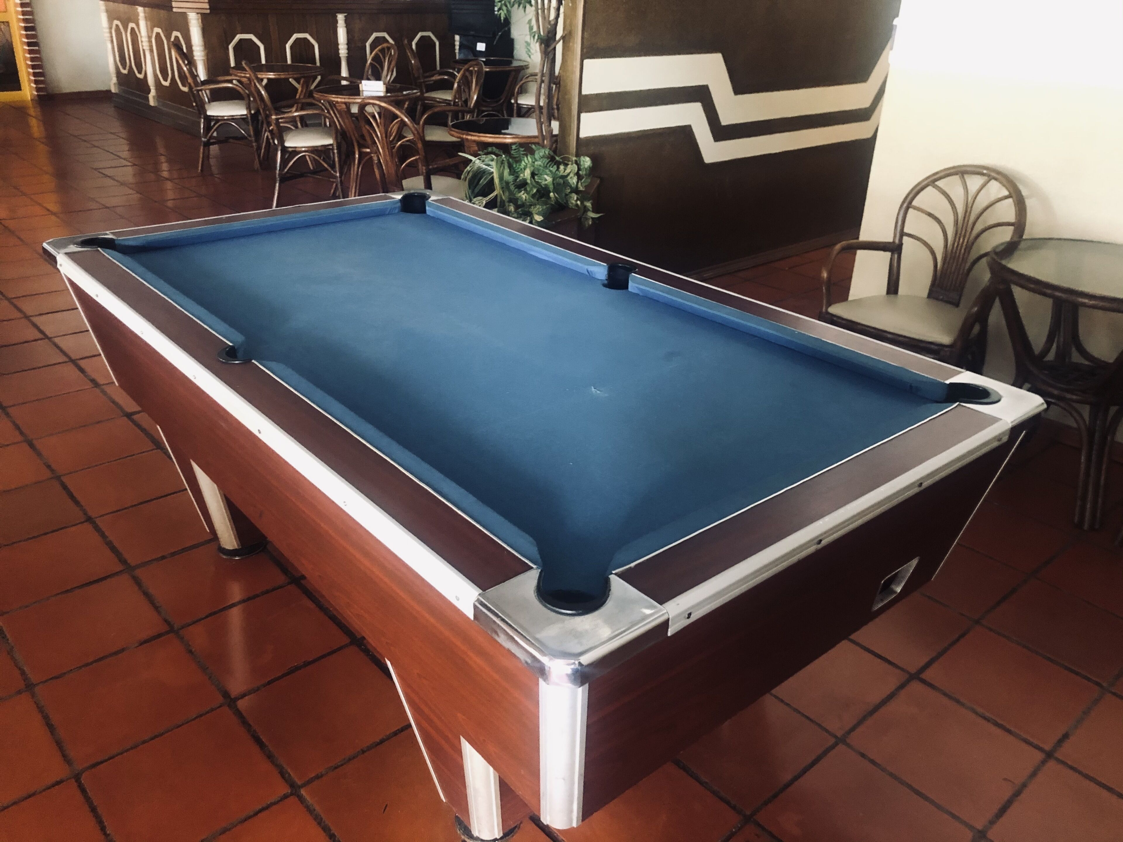 A pool table in a room with tiled flooring and wicker furniture.