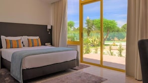 A bedroom with a large bed, a nightstand, and a view of a garden through a sliding glass door. - Hotel Pinhal do Sol (Loulé)