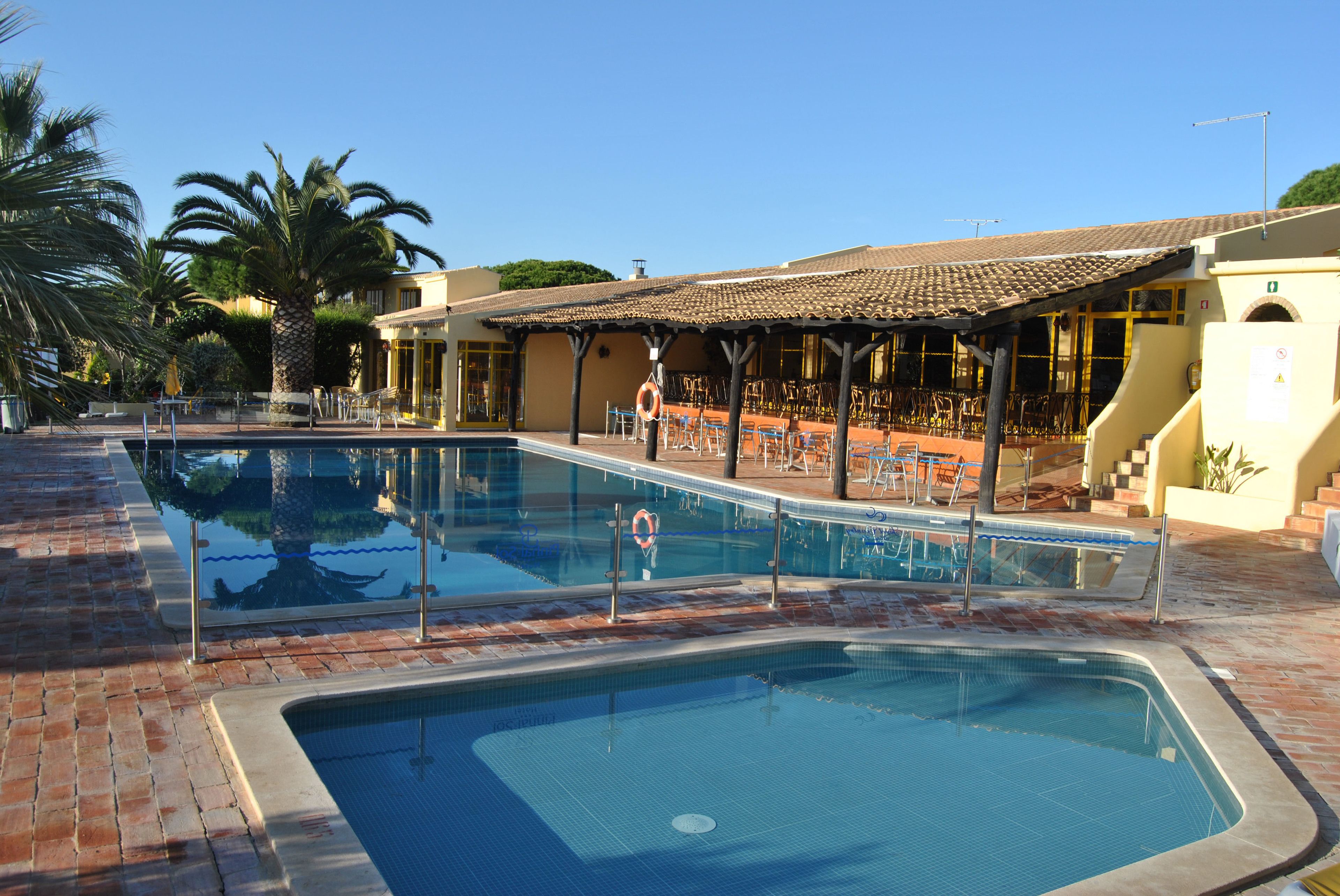 A swimming pool with a tiled deck, surrounded by lounge chairs and a covered seating area.