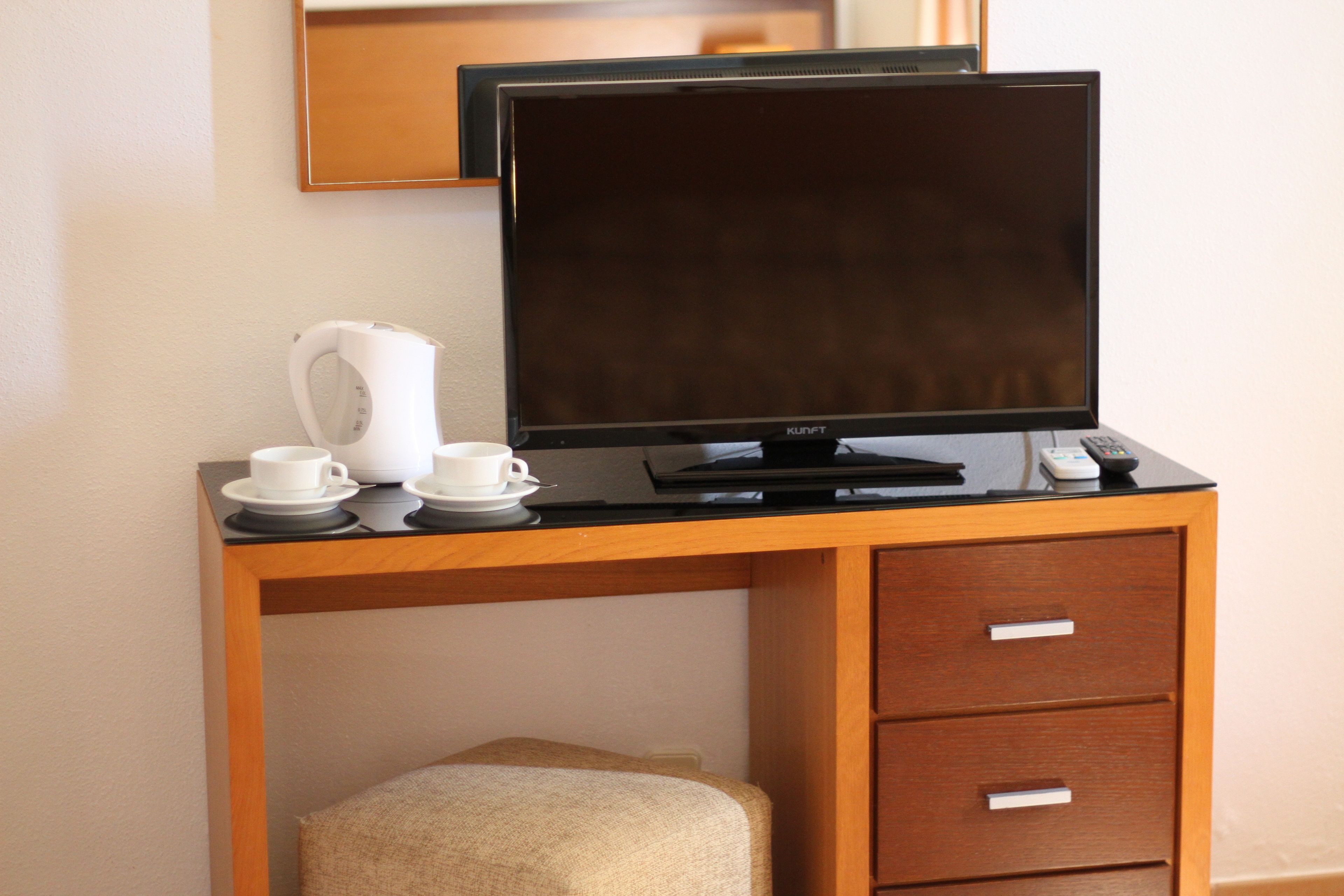 Un escritorio de hotel con un monitor de pantalla plana, una cafetera y un control remoto.