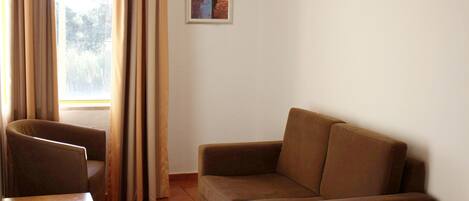 A room with a brown sofa, a chair, a small table, and a window with curtains.