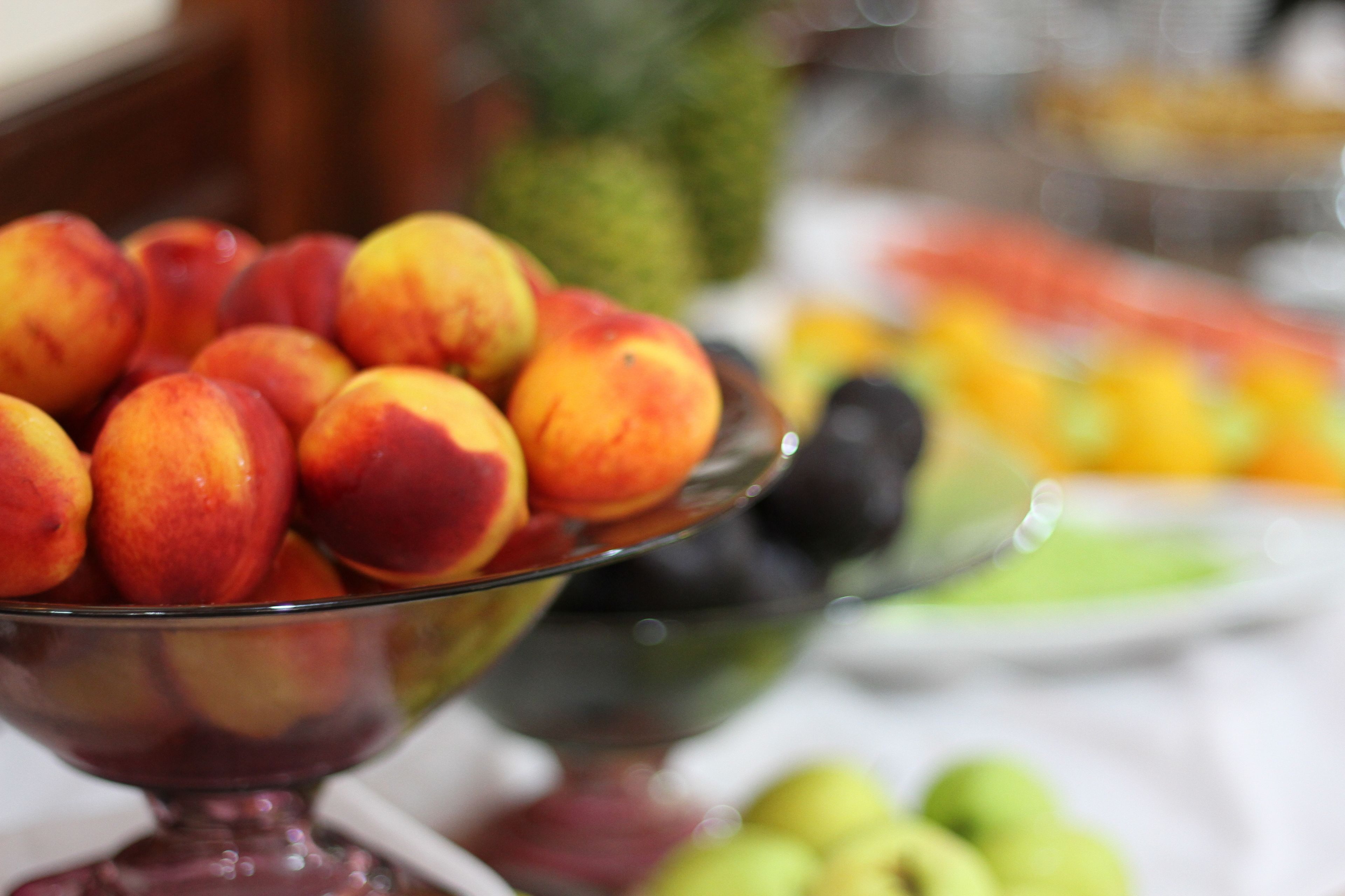 A glass bowl filled with peaches and other fruits.